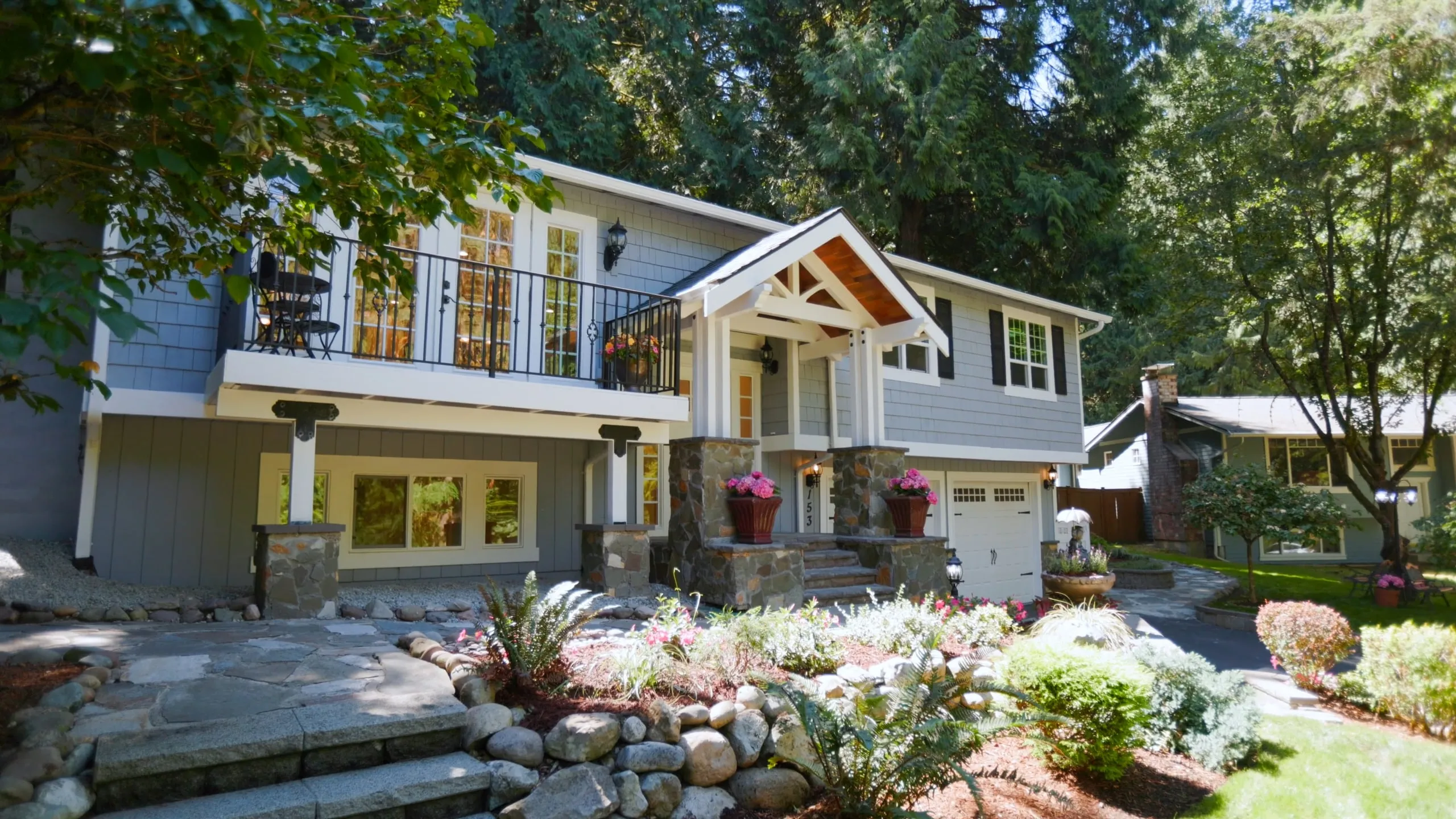Split-level home with a covered balcony and stone steps under mature trees, the opening frame of a listing film