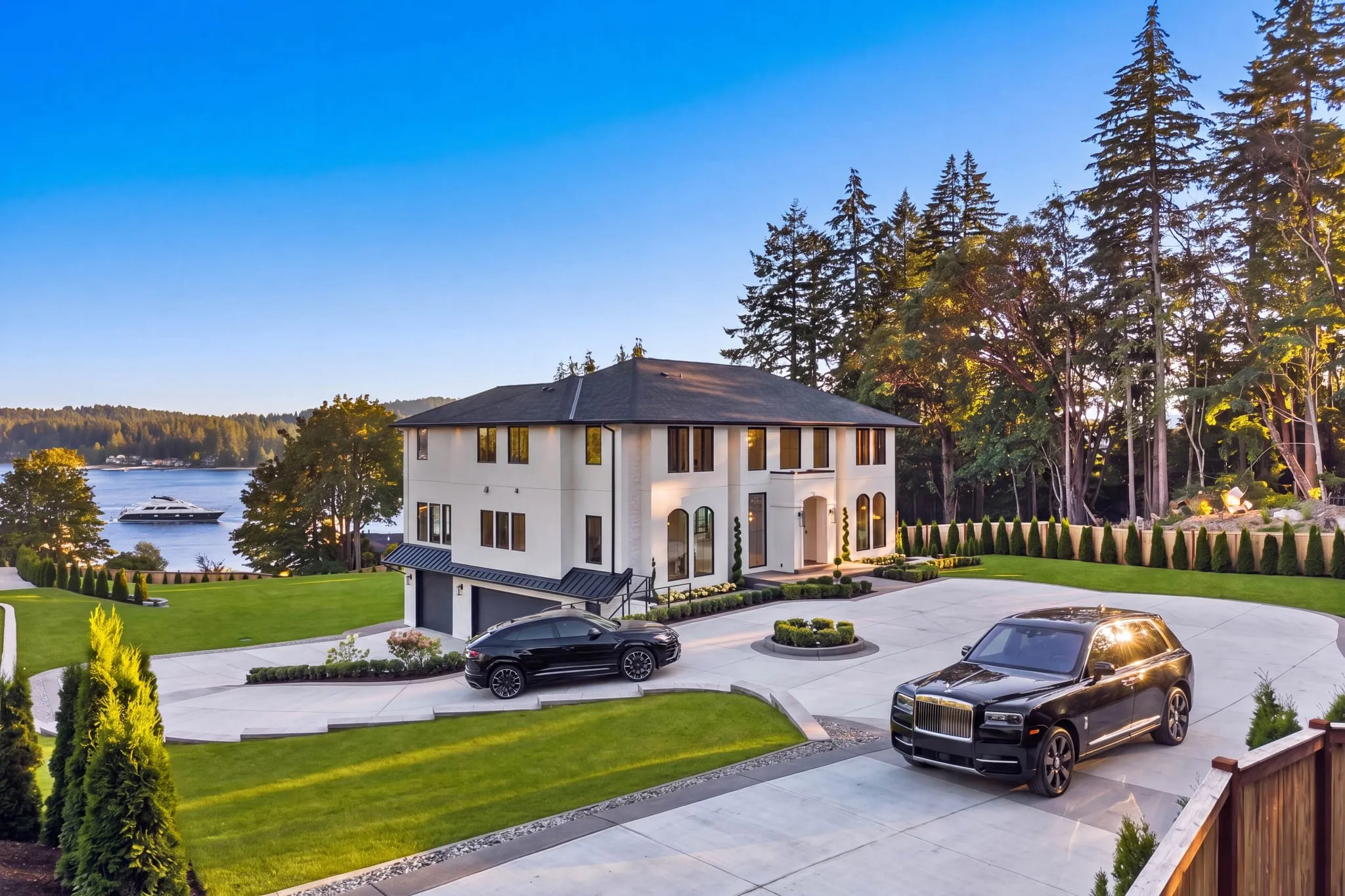 Aerial view of a white waterfront estate with a circular drive at dusk, photographed by ACRE Seattle