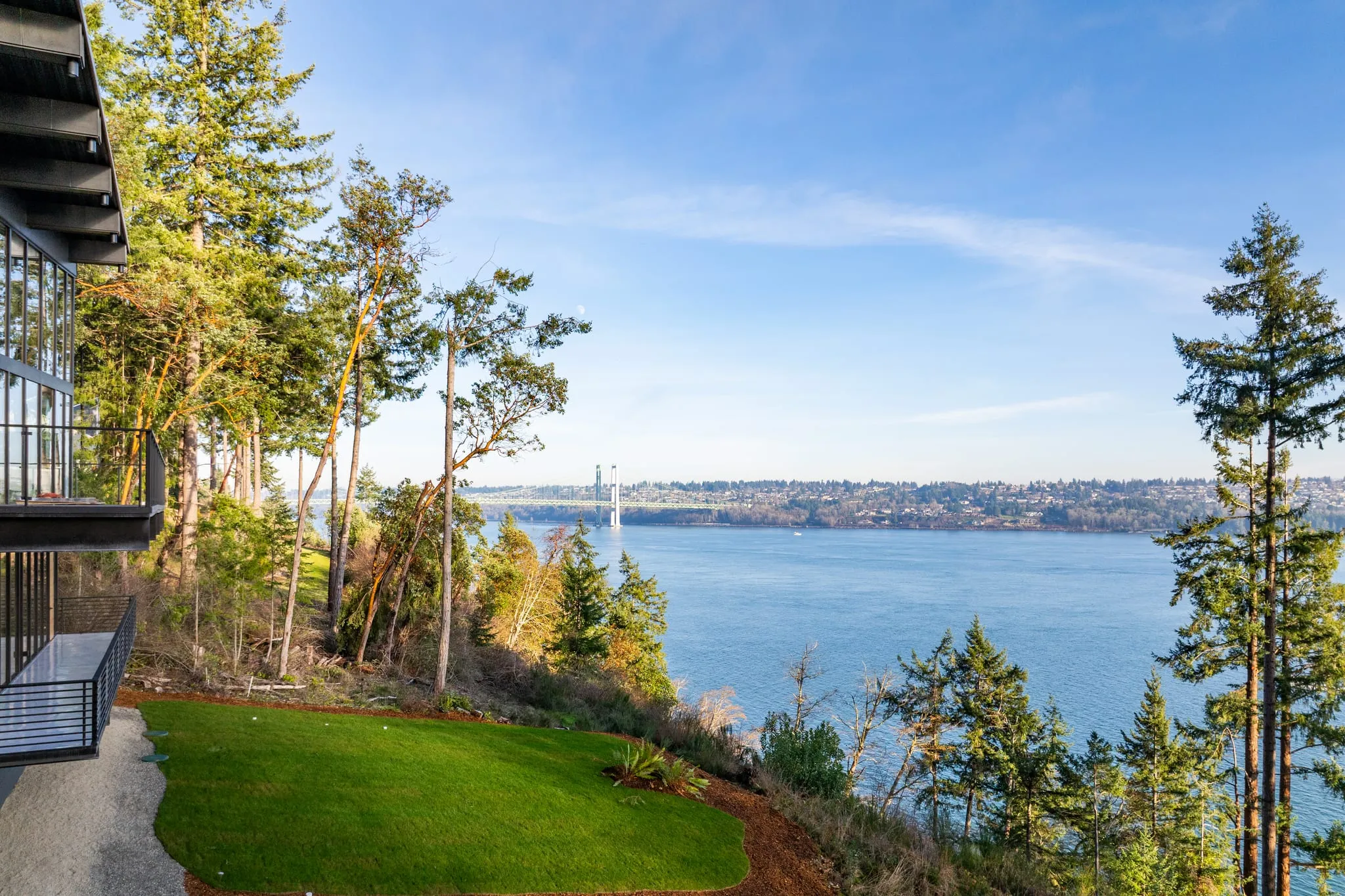 Bluff-top lawn beside a glass-walled home overlooking Puget Sound and the Narrows Bridge, photographed by ACRE Seattle