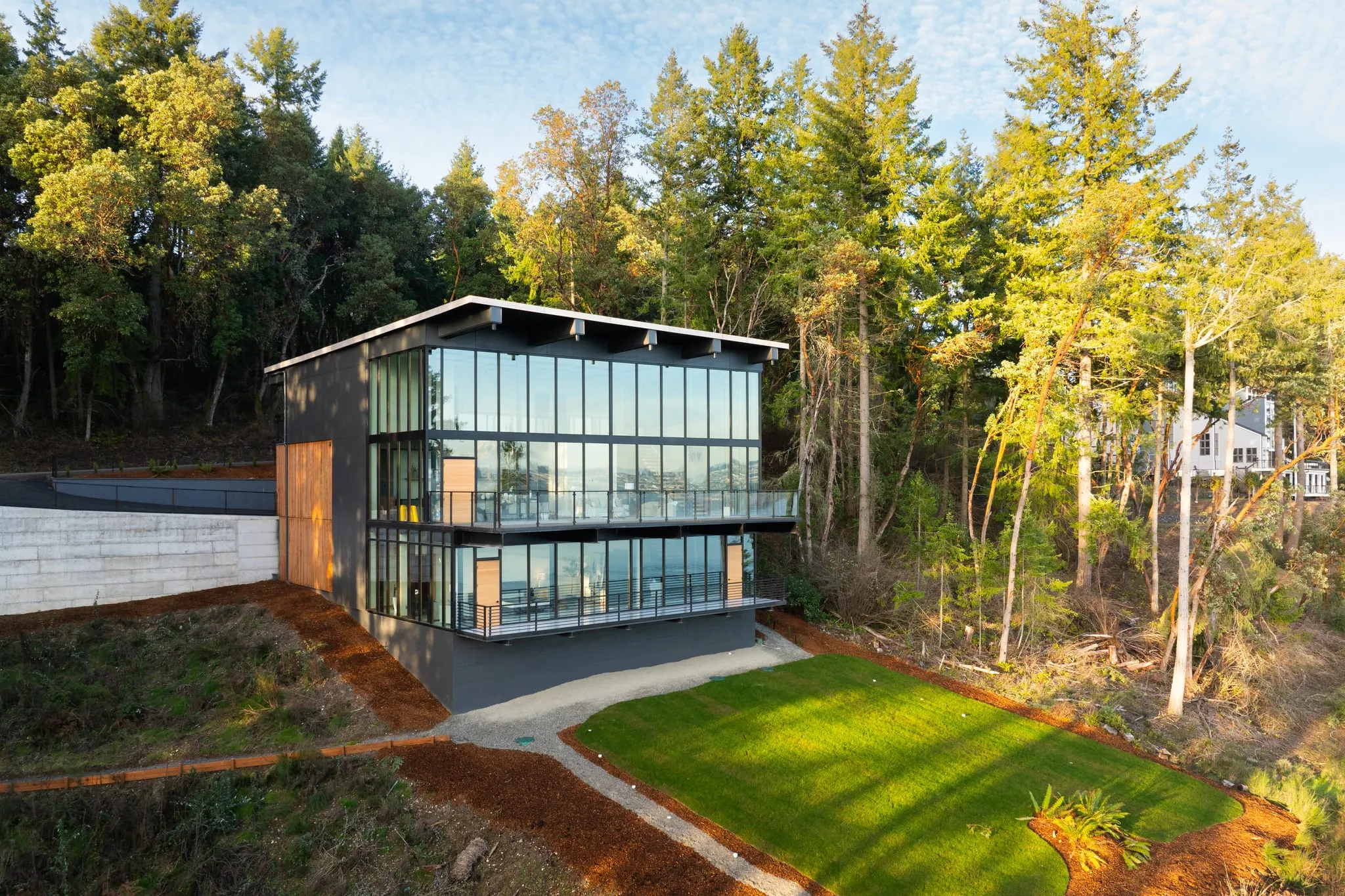 Glass-walled modern home set among evergreens, shot from above at sunrise by ACRE Seattle