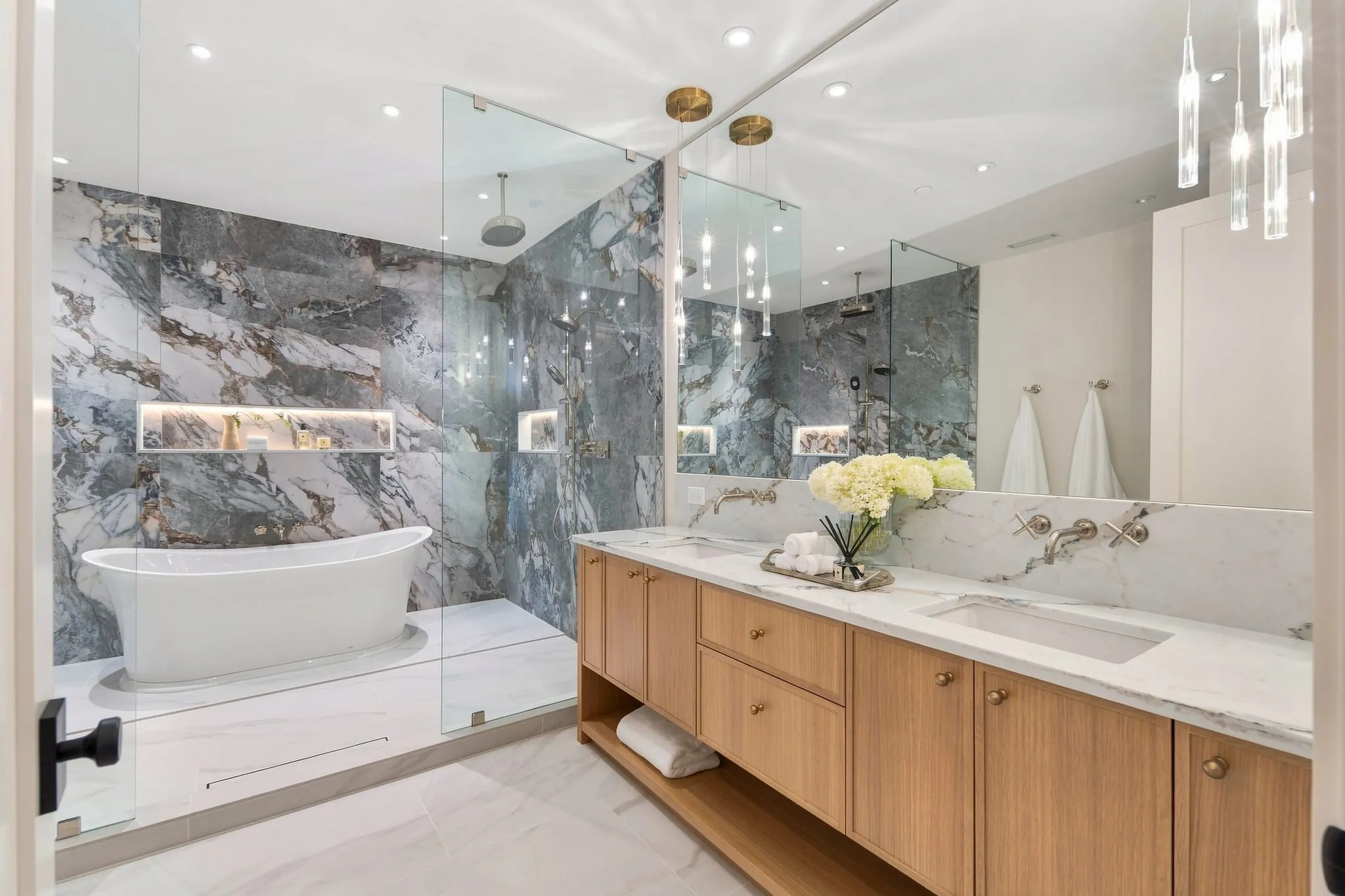Primary bath wrapped in dramatic gray marble with a freestanding tub and oak vanity