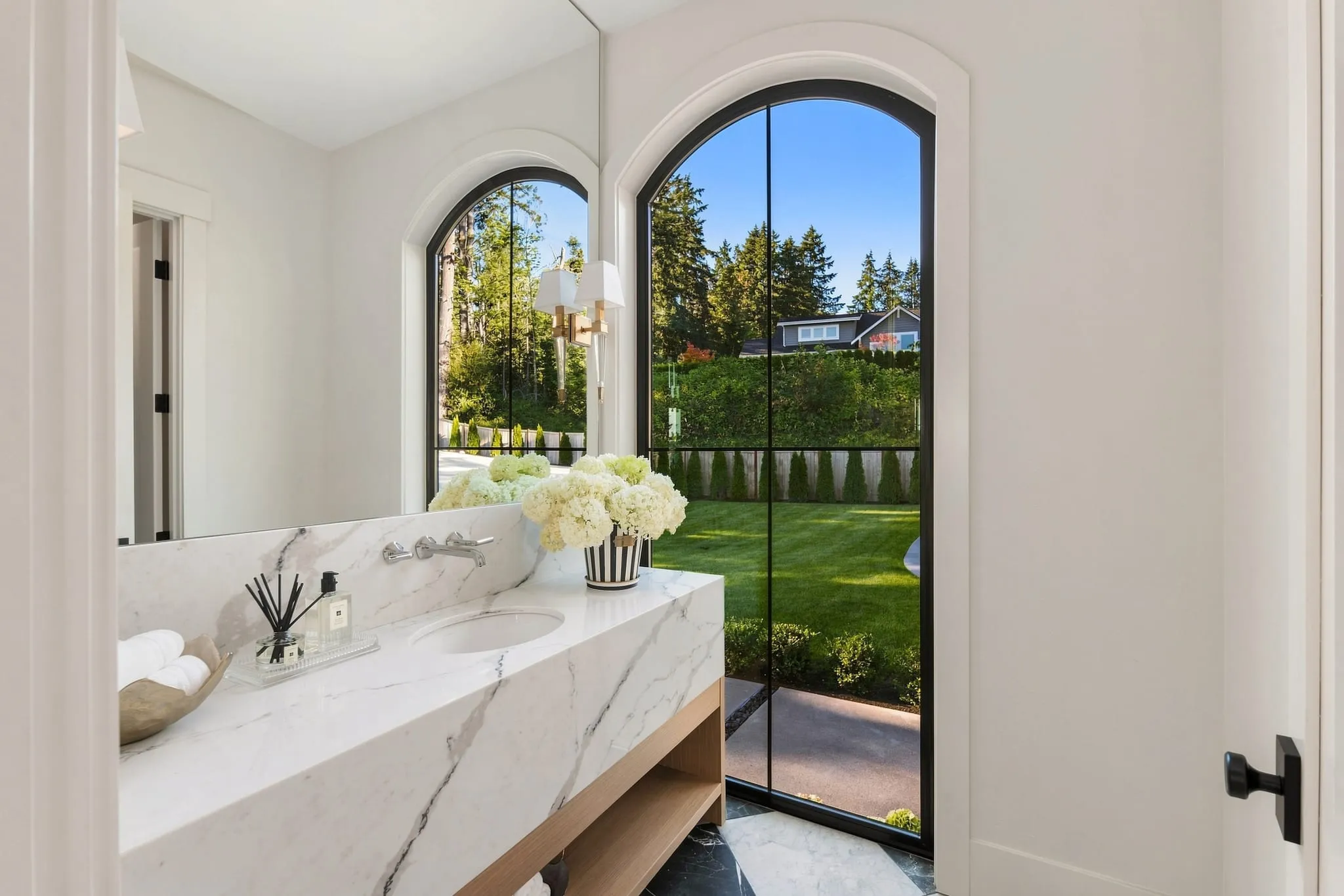 Powder room with a marble vanity and an arched window onto the garden