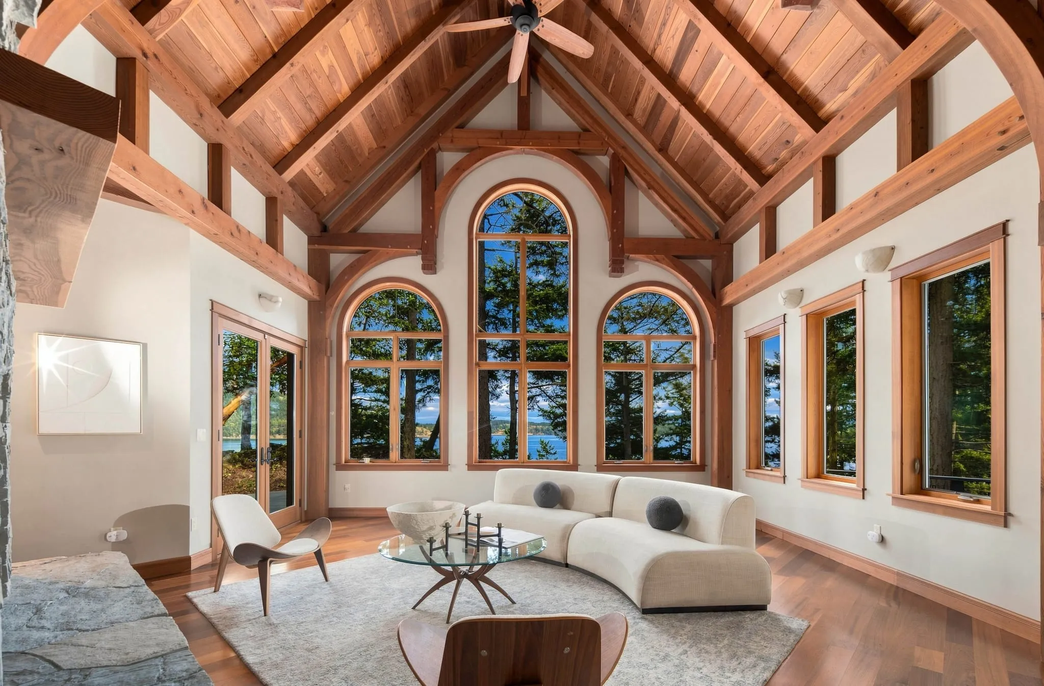 Timber-frame great room with a vaulted wood ceiling, arched windows and a curved white sofa