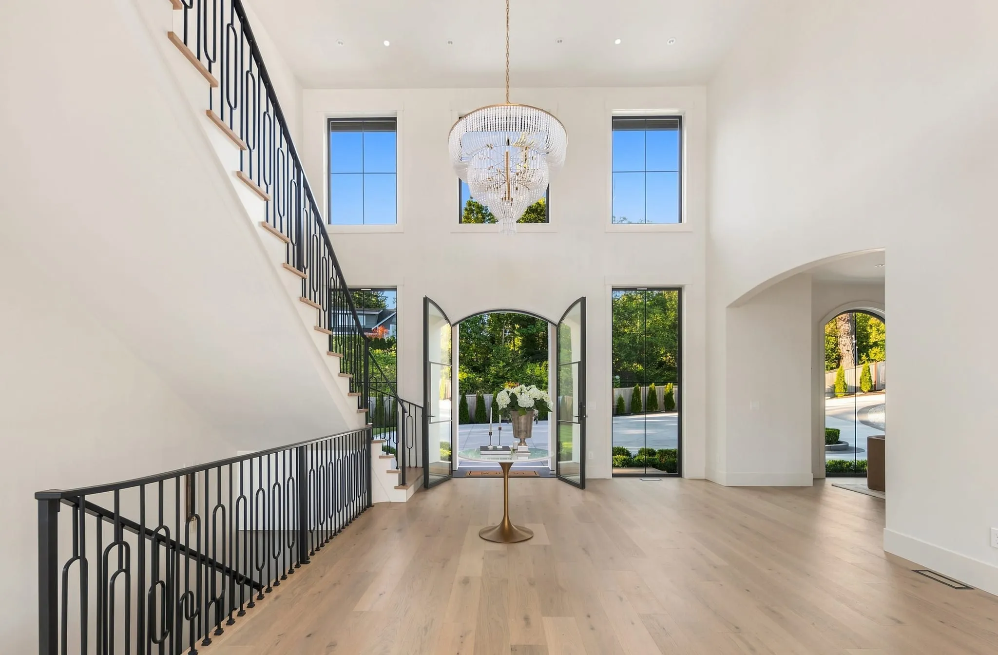 Double-height foyer with a beaded chandelier, iron stair rail and open glass doors