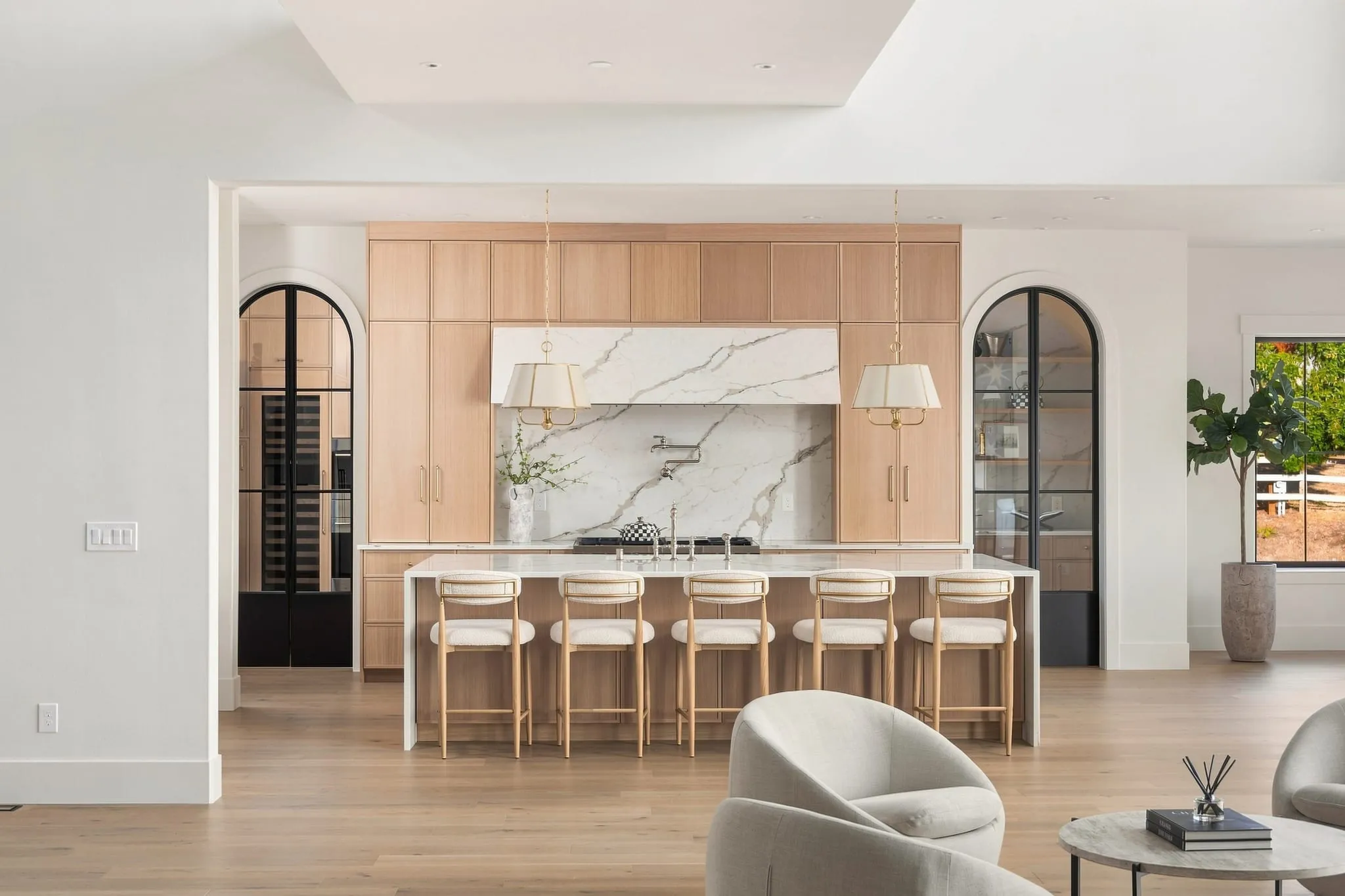 White oak kitchen with a marble hood and backsplash, brass pendants and island seating
