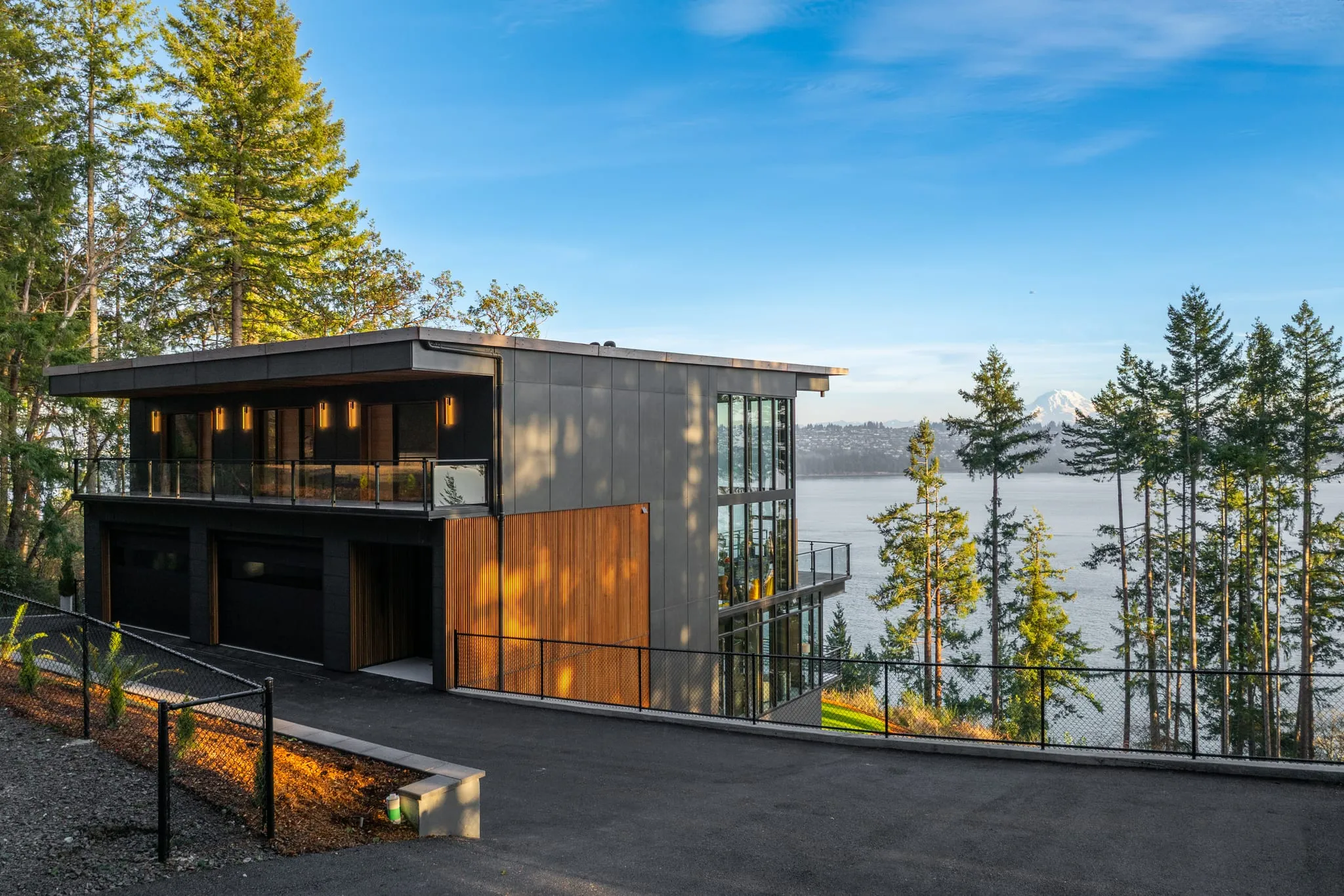 Modern dark-clad waterfront home at golden hour with Mount Rainier across the water, photographed by ACRE Seattle