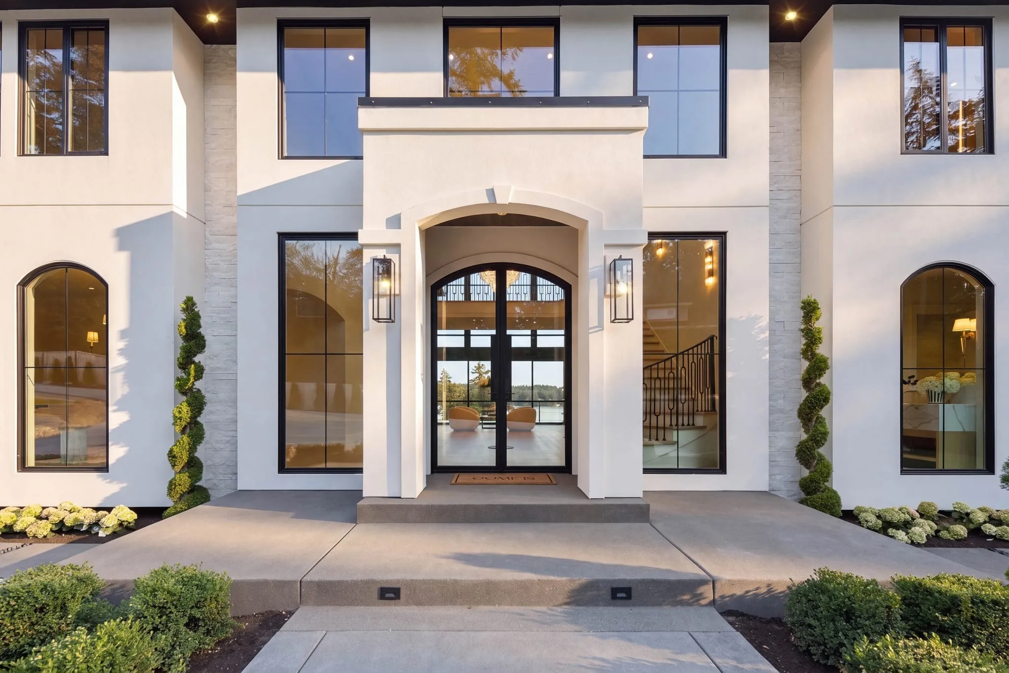 Arched double-door entry of a white estate at golden hour, photographed by ACRE Seattle