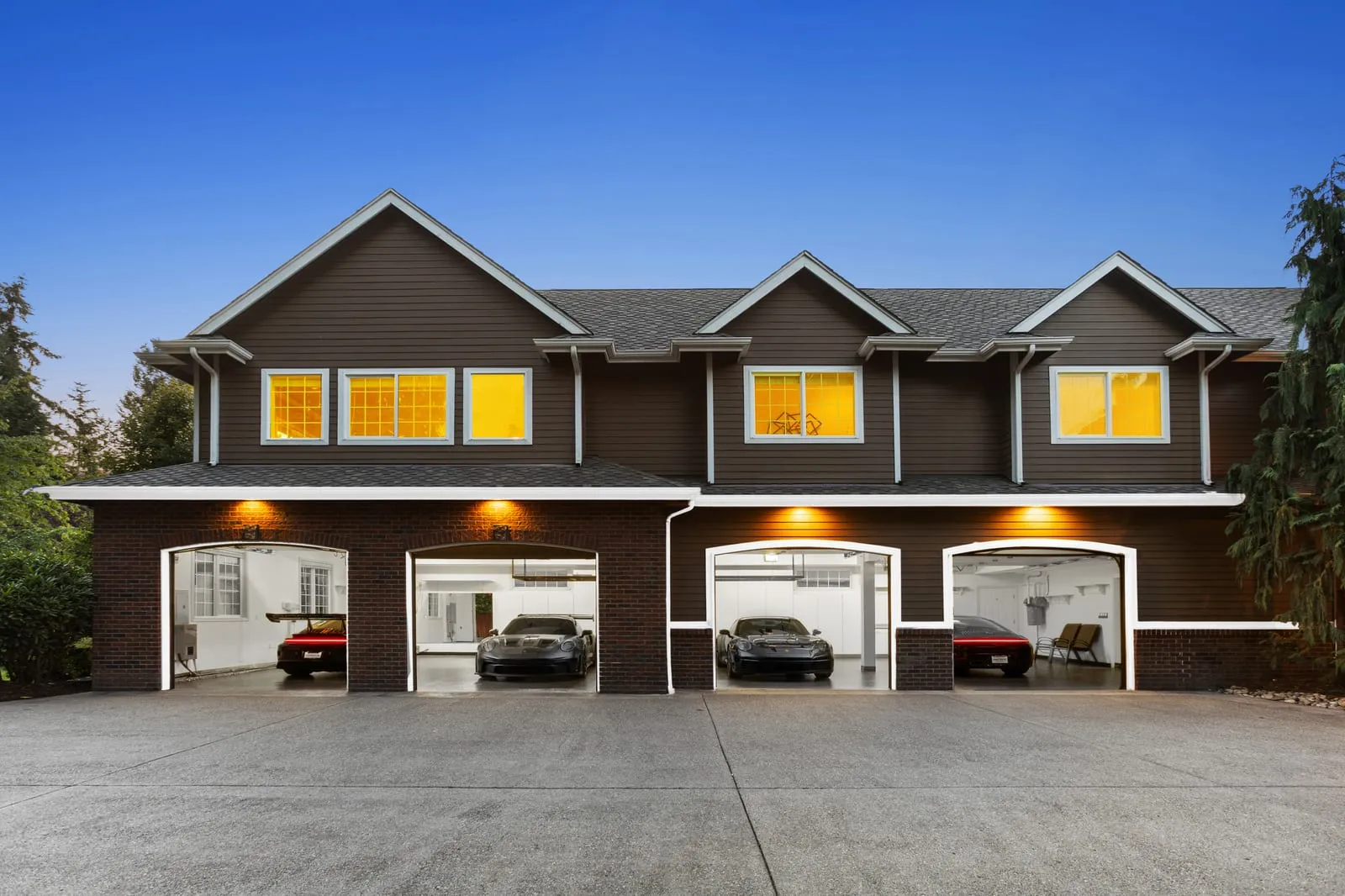 Row of dark-sided townhomes at dusk, every window lit and the garage bays glowing