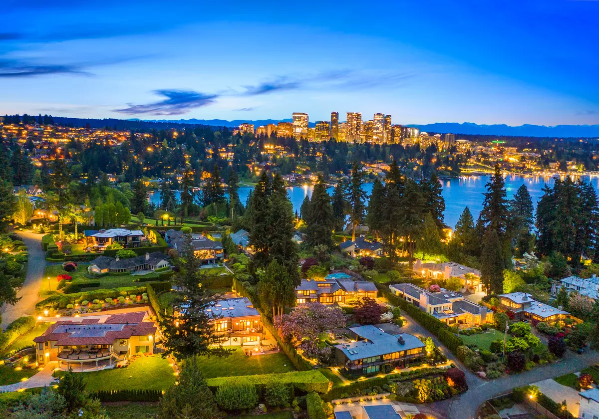 Aerial view over Lake Washington at twilight, waterfront homes lit along the shoreline with the Bellevue skyline beyond