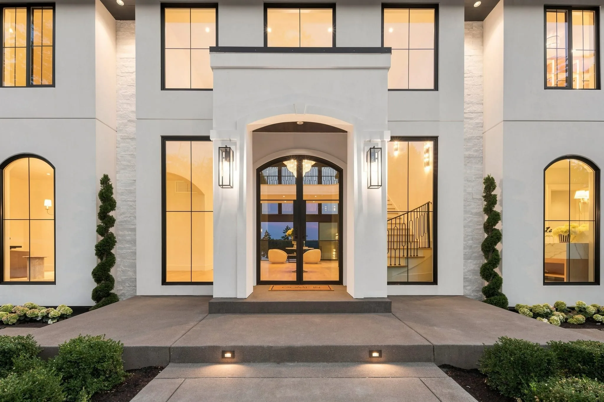 Grand arched entry at dusk flanked by spiral topiaries