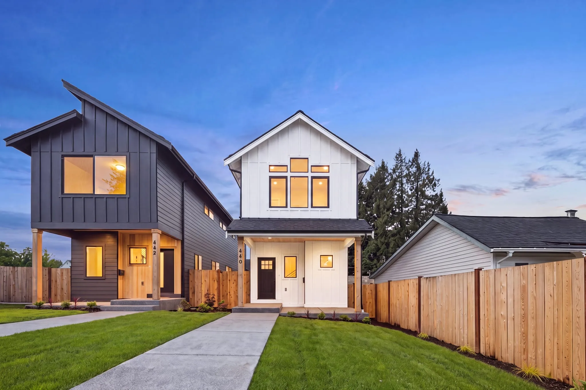 Two new-construction homes glowing at twilight, photographed by ACRE Seattle for a twilight set