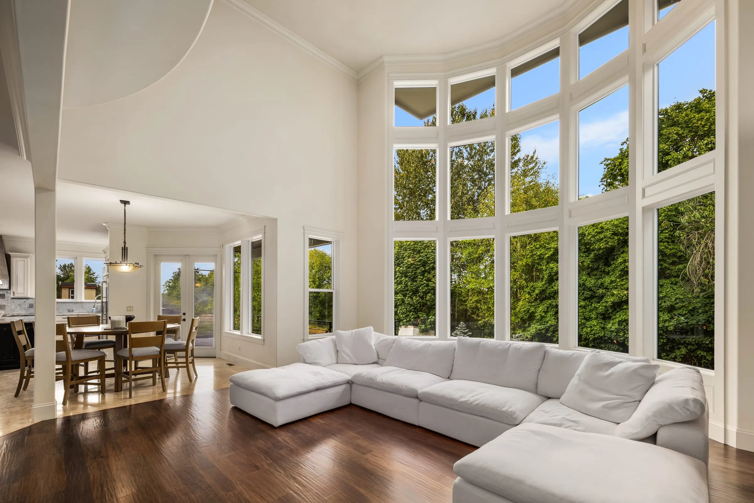 Double-height great room with a curved two-storey window wall looking onto evergreens